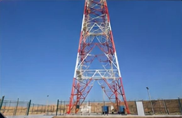 Relocated red and white lattice watchtower inside its fenced compound